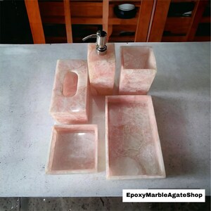 May include: A bathroom set made of pink agate with a soap dispenser, a tissue box, a tray, and two small dishes.