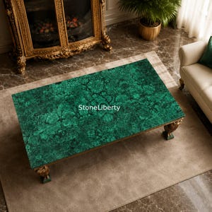 Puede incluir: Una mesa de centro rectangular con una superficie de patrón de malaquita verde vibrante con vetas oscuras intrincadas. La mesa tiene patas doradas ornamentadas y el texto StoneLiberty está impreso en blanco en el centro de la superficie.