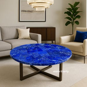 May include: A round coffee table with a vibrant blue mosaic top. The table has a dark brown metal base with an X-shaped design. The table is in a living room setting with a sofa and armchair.