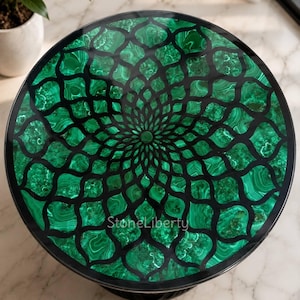 Puede incluir: Una mesa redonda con un tablero que presenta una incrustación de malaquita verde dispuesta en un patrón floral geométrico repetitivo separado por finas líneas negras. El centro del tablero muestra el texto StoneLiberty en letra clara.
