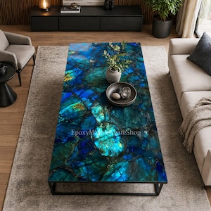 May include: A rectangular coffee table with a striking blue and green marbled surface. The table has a black metal frame and is decorated with a small vase, a bowl, and decorative items. The text "EpoxyMarbleSlateShop" is visible.