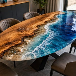 Può includere: Un tavolo da pranzo ovale caratterizzato da una lastra di legno naturale con bordo vivo e un inserto in resina blu che imita le onde dell'oceano, completo di dettagli in schiuma bianca, conchiglie incastonate e base in metallo nero, testo StoneLiberty.