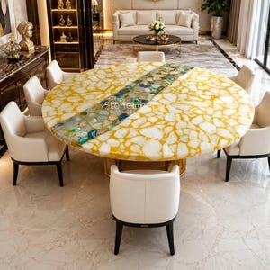May include: A circular dining table with a yellow and white patterned surface, featuring a central strip of blue and green stones. The table is surrounded by white chairs with dark legs, in a bright room.