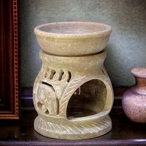 Könnte beinhalten: Ein geschnitzter Öllampenbrenner aus Stein mit einem komplizierten Design aus Blättern und einem Elefanten. Der Brenner ist aus hellem braunem Stein gefertigt und hat oben eine kleine Schale zum Aufnehmen von Öl.