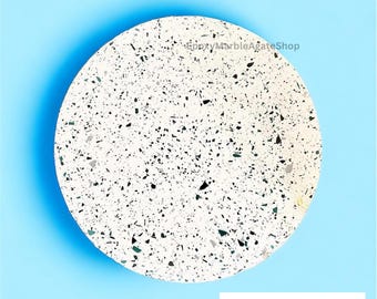 Pode incluir: Um coaster redondo de terrazzo branco com manchas pretas e verdes. O coaster está sobre um fundo azul claro. EpoxyMarbleAgateShop