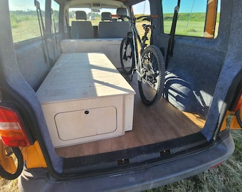 May include: The interior of a van with a wooden bed platform and a bicycle stored in the back. The van is painted yellow and has a gray carpet lining the interior.