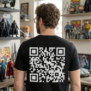 Puede incluir: Una camiseta negra de manga corta con un código QR cuadrado de color blanco estampado en la espalda. El diseño consiste en una cuadrícula estándar de cuadrados pequeños y cuadrados más grandes en las esquinas, centrada en la tela.
