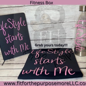 Puede incluir: Un conjunto temático de fitness que incluye un cuaderno negro, una camiseta negra y una botella de agua transparente. El cuaderno y la camiseta tienen el texto "Life Style starts with Me" en rosa. La botella de agua también tiene la palabra "Life Style" en rosa.