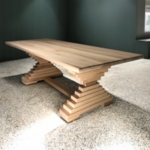 Op de afbeelding: Een houten eettafel met een natuurlijke afwerking en een unieke basis gemaakt van gestapelde houten planken. De tafel heeft een rechthoekig blad en een brede, stevige basis.