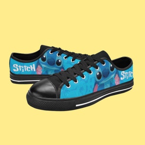 May include: A pair of black canvas low-top trainers with a blue and white print featuring Stitch from Lilo & Stitch. The print includes the word "Stitch" on both shoes.