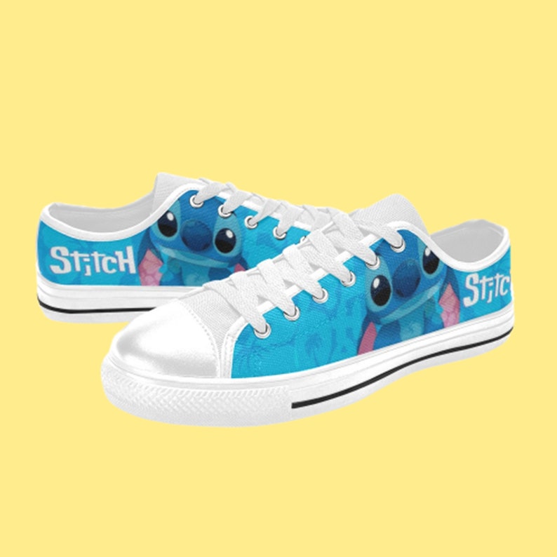 May include: White canvas low-top trainers with a blue and white design featuring Stitch from Lilo & Stitch. The shoes have white laces and the word "Stitch" is printed on the side.