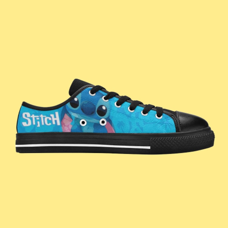 May include: Black canvas low-top trainers with a blue and white print featuring Stitch from Lilo & Stitch. The print includes the word "Stitch" on the side of the shoe.