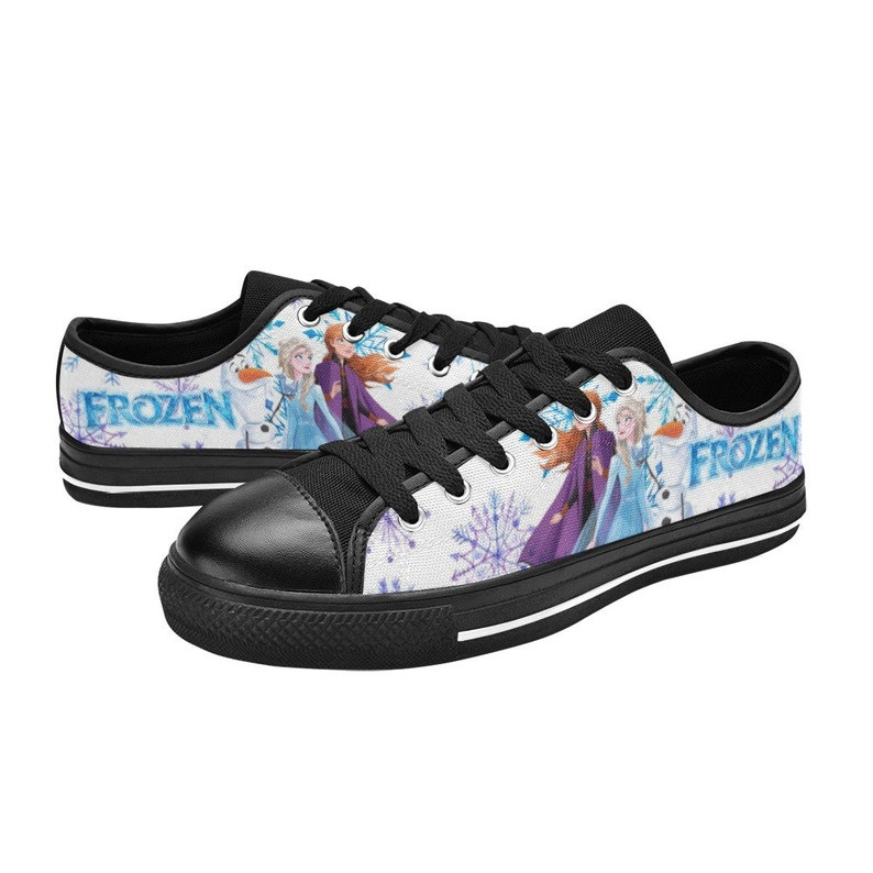 May include: Black canvas low-top sneakers with a white background featuring a Frozen design with Elsa and Anna. The shoes have black laces and a white stripe around the sole. The words "Frozen" are printed on the side of the shoes.