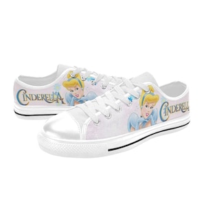 May include: White canvas low-top trainers with a pink and white background featuring Cinderella in a blue dress and the word "Cinderella" in pink lettering.