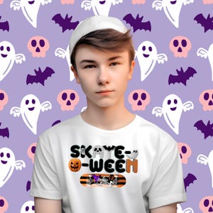 Puede incluir: Una persona joven que lleva una camiseta blanca con un gráfico de una patineta y el texto "Skate-oween". La persona lleva una gorra de béisbol blanca y está de pie frente a un fondo morado con un patrón de fantasmas y murciélagos.