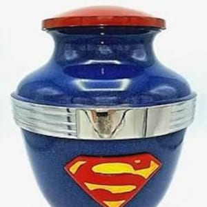 Può includere: Urna crematoria in ceramica blu e rossa con base e coperchio argentati. L'urna presenta un logo Superman.