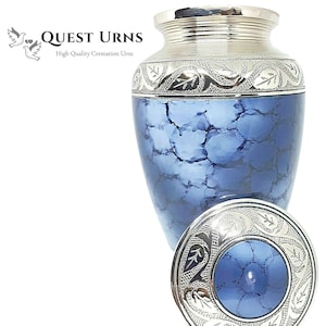 May include: A silver and blue cremation urn with a decorative floral design. The urn has a lid with a matching design.