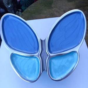 Op de afbeelding: Een zilveren serveerschaal in de vorm van een vlinder met twee blauwe en twee turquoise secties.