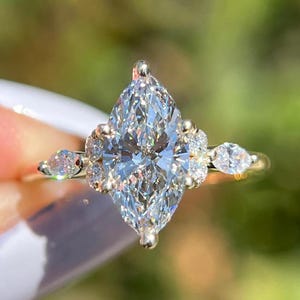 Stunning cluster marquise-cut diamond ring set in white gold, featuring a brilliant marquise center stone surrounded by round accent diamonds for a dazzling effect. This elegant engagement ring blends vintage charm with modern elegance, making it an ideal choice for brides, anniversaries, or fine jewelry lovers. The cluster setting enhances the sparkle, creating a luxurious and timeless look. Crafted with high-quality materials, this ring is perfect for stacking, weddings, or special occasions.