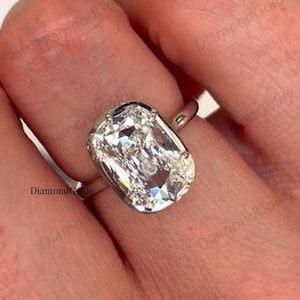 May include: A close-up of a hand wearing a silver ring with a large, rectangular, clear gemstone. The ring's band is thin and simple, and the gemstone is set in a bezel setting. The ring is a piece of jewelry.