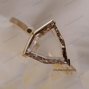 May include: A gold ring with a clear, faceted gemstone set in a geometric, triangular shape.