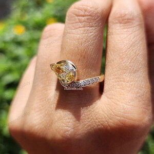 May include: A gold ring featuring a pear-shaped yellow diamond as the primary stone. The ring has a curved design with a row of smaller, clear diamonds set along the band. The ring is on a finger.