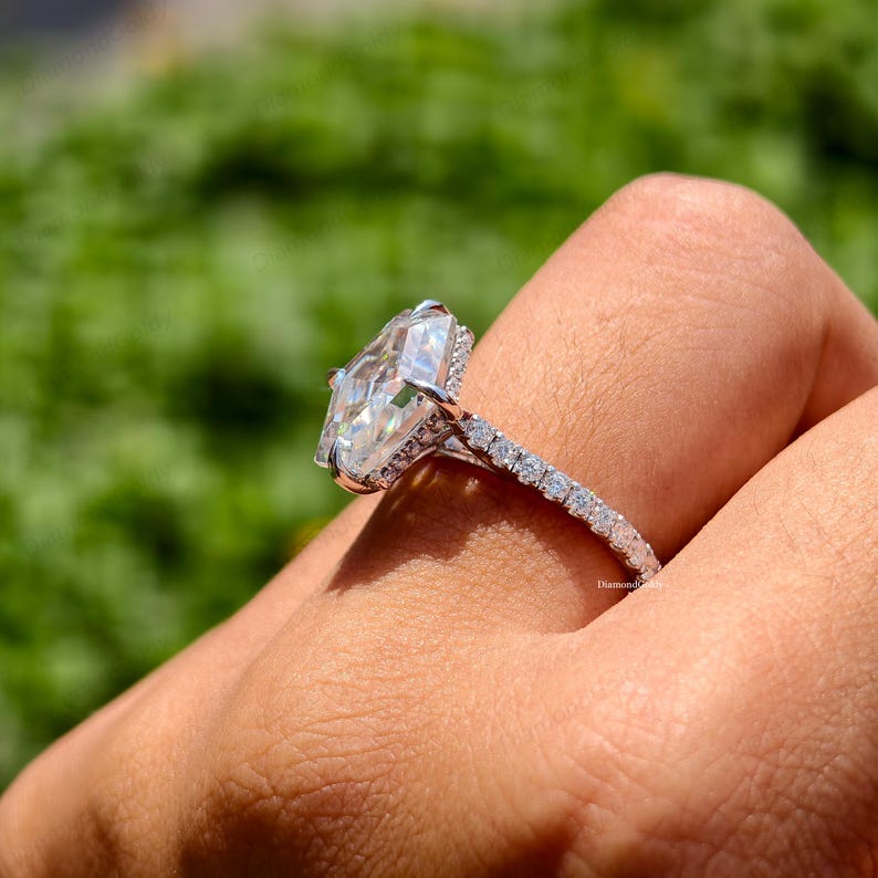 May include: A silver ring with a large, clear, rectangular-cut gemstone. The band is encrusted with small, sparkling stones. The ring is set against a blurred green background.