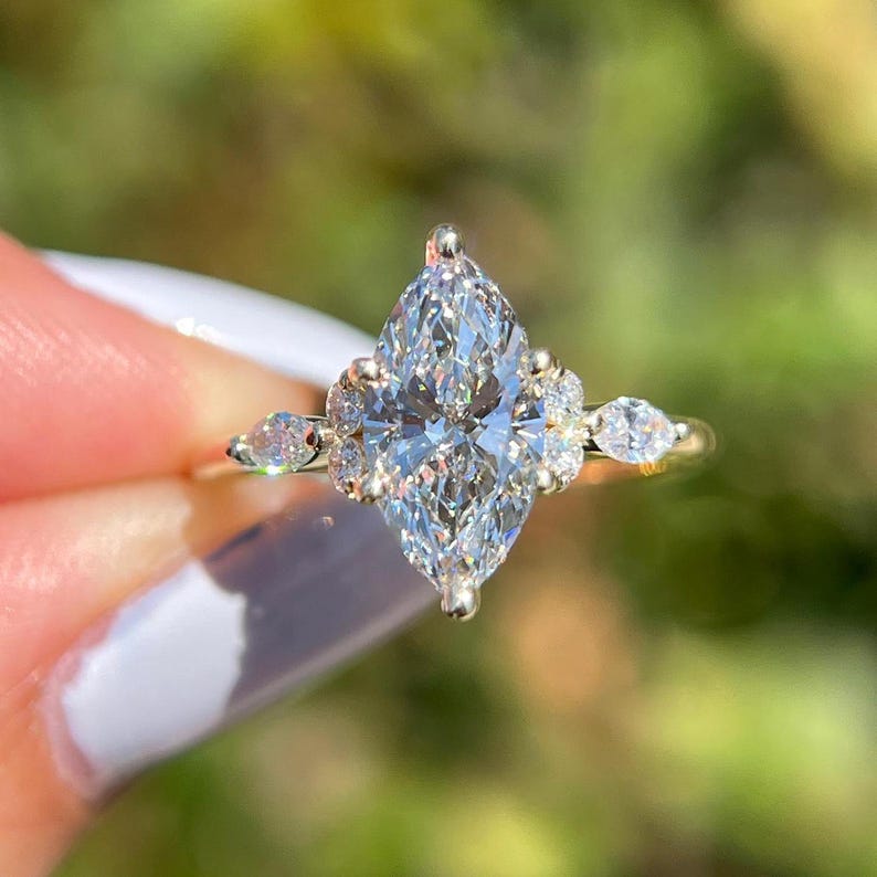 Stunning cluster marquise-cut diamond ring set in white gold, featuring a brilliant marquise center stone surrounded by round accent diamonds for a dazzling effect. This elegant engagement ring blends vintage charm with modern elegance, making it an ideal choice for brides, anniversaries, or fine jewelry lovers. The cluster setting enhances the sparkle, creating a luxurious and timeless look. Crafted with high-quality materials, this ring is perfect for stacking, weddings, or special occasions.