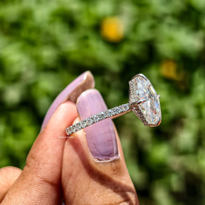 May include: A silver engagement ring with a large, clear, oval-cut diamond as the centerpiece. The band is encrusted with small, sparkling diamonds. The ring is held up against a blurred green background.