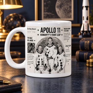 Peut inclure: Un mug en céramique blanche orné d'un graphisme style journal intitulé Apollo 11 Humanity's Giant Leap. Le design comprend des photos en noir et blanc de trois astronautes en combinaison spatiale, du texte sur l'alunissage et le logo Daily Herald.