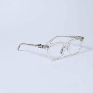 May include: Clear plastic spectacles with silver metal accents on the arms. The glasses have a square frame.
