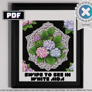 Puede incluir: Un patrón de punto de cruz enmarcado con un diseño floral de hortensias rosas, moradas y azules sobre un fondo negro, con un borde de encaje blanco. El texto "SWIPE TO SEE IN WHITE AIDA" es visible.