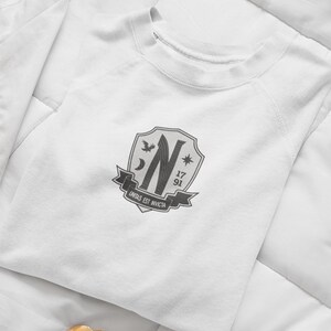 May include: White sweatshirt with a gray crest featuring a stylized letter N, a crescent moon, a star, a bird, and the text "unitas est invicta". The crest also includes the numbers 17 and 91.