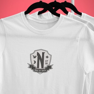 May include: White t-shirt with a black and gray crest featuring a stylized "N", a crescent moon, a star, a bird, and the text "17 91 UNITAS EST INVICTA".