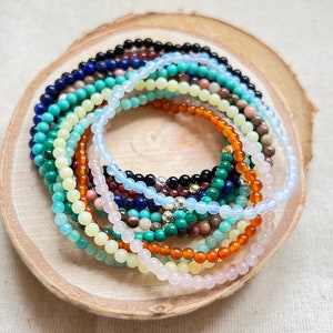 May include: A collection of colourful gemstone bracelets stacked on a wooden surface. The bracelets are made of various stones, including turquoise, carnelian, rose quartz, and amethyst.