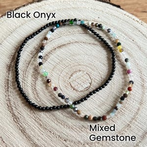 May include: Two bracelets, one black onyx and one with mixed gemstones. The bracelets are layered on top of each other on a wooden surface.