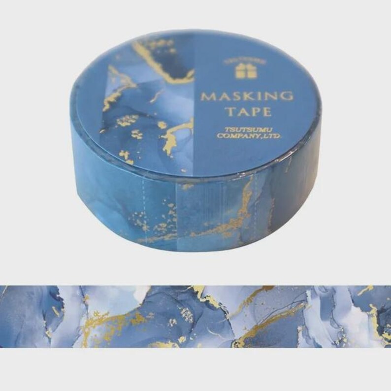May include: A roll of blue masking tape featuring a marbled pattern with gold foil accents. The label on the roll displays the text MASKING TAPE and TSUTSUMU COMPANY, LTD. A strip of the tape is shown below the roll, displaying the same blue and gold design.