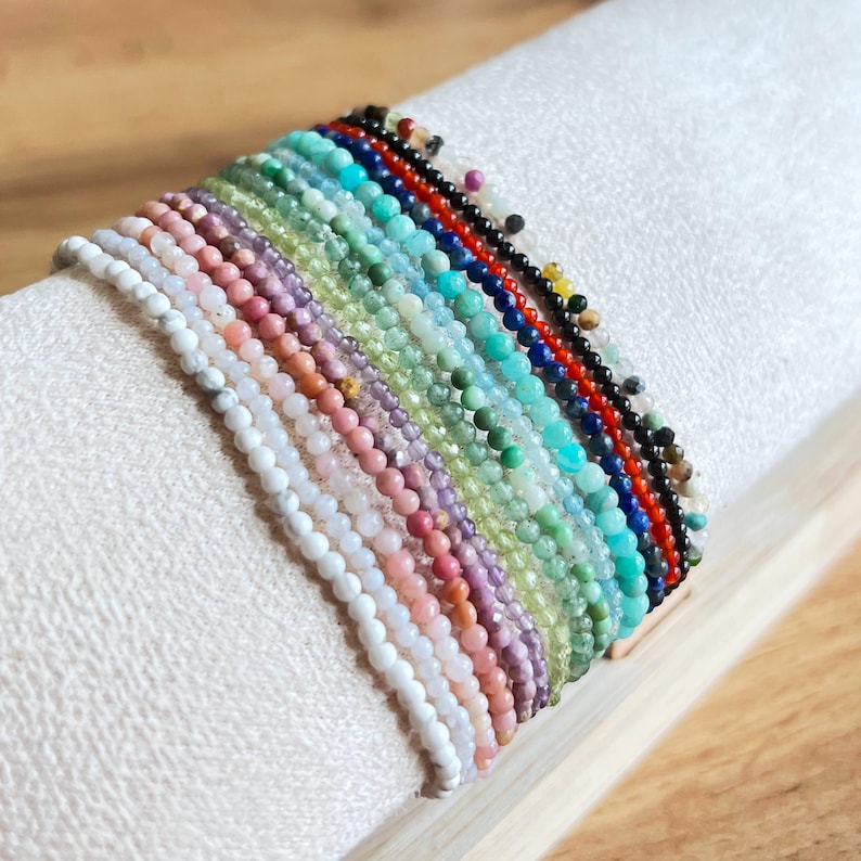 May include: A collection of 20 colorful gemstone bracelets, each featuring a different type of stone. The bracelets are stacked on top of each other, showcasing the variety of colors and textures.