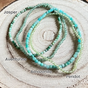 May include: Four strands of gemstone bracelets in shades of green, including jasper, aventurine, amazonite, and peridot.