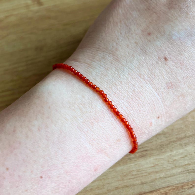May include: A delicate bracelet made with small, bright orange carnelian beads.