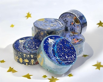 May include: A collection of five rolls of masking tape featuring a dark blue night sky theme with gold stars, celestial patterns, and the text Shinzi Katoh 15mm x 3m. The rolls are arranged in a cluster, showcasing various illustrations of birds and plants.