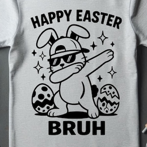 May include: Light gray t-shirt with a black graphic of a bunny wearing sunglasses and a hat, dabbing. The text reads "HAPPY EASTER BRUH" with star accents and Easter eggs.
