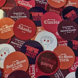 Könnte beinhalten: Eine Sammlung runder Aufkleber mit verschiedenen Motiven, darunter Texte wie The Vampire Lestat, Interview with the Vampire, My coven is Claudia, I have the blood of Akasha in me und I am the Devil's Minion, sowie stilisierte Gesichter.