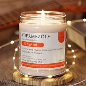 May include: A clear glass candle jar with a white label that reads "ATIPAMEZOLE flammable solution 5 mg/mL whale fumes to reverse sleepiness and sedation, and to wake your ass up. Keep in a safe place. Not to be centrifuge or oxygen tank. Rx only For veterinary use only Rapid onset of reversed sleepiness for veterinary professionals."