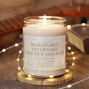 May include: A white soy wax candle in a clear glass jar with a brown wooden lid. The label reads "World's Best Veterinary Practice Manager" with the text "Vegan Soy Wax Candle" and "For Veterinary Professionals".