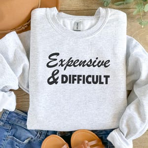 May include: A gray sweatshirt with the text "Expensive & Difficult" printed in black.