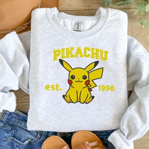 May include: A gray sweatshirt with a yellow Pikachu graphic and the text "Pikachu est. 1996".
