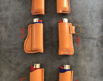 May include: Six leather lighter cases in various styles. The cases are all brown leather with contrasting stitching. Some cases have a key ring attached.