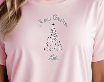 Könnte beinhalten: Hellrosa T-Shirt mit dem Text "Merry Christmas" über einem gepunkteten Weihnachtsbaum-Design. Der Name "Skyla" ist darunter aufgedruckt. Das Shirt hat einen lässigen Stil.