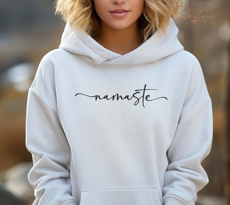 K&ouml;nnte beinhalten: Wei&szlig;er Kapuzenpullover mit dem Wort "namaste" in schwarzer Kursivschrift.